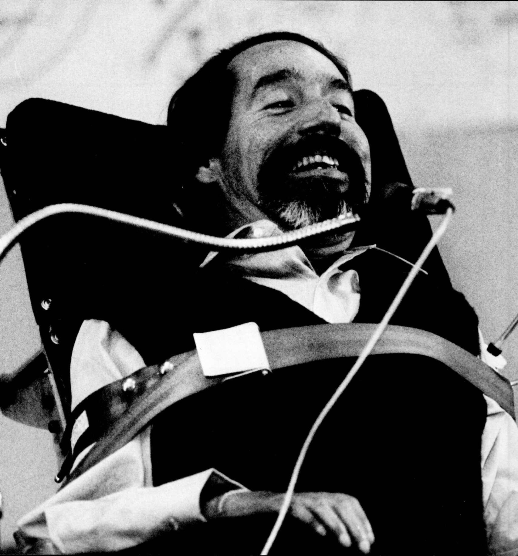 Image of Ed Roberts smiling secured to his electric wheelchair. Photographer: William Bronston